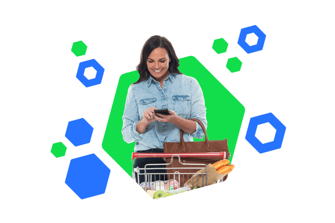 Eine lächelnde Frau in einem Jeanshemd benutzt ihr Smartphone, während sie einen Einkaufswagen voller Lebensmittel schiebt. Der bunte, hexagonale Hintergrund verstärkt die fröhliche und moderne Atmosphäre des Einkaufserlebnisses.