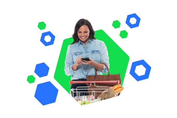 Eine lächelnde Frau in einem Jeanshemd benutzt ihr Smartphone, während sie einen Einkaufswagen voller Lebensmittel schiebt. Der bunte, hexagonale Hintergrund verstärkt die fröhliche und moderne Atmosphäre des Einkaufserlebnisses.